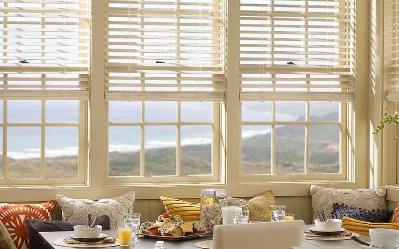 Lutron motorized shades partially lowered over large windows in a sunlit breakfast room