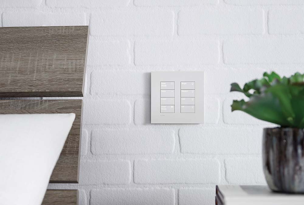 White Lutron Palladiom 8-button keypad mounted on a white brick wall.