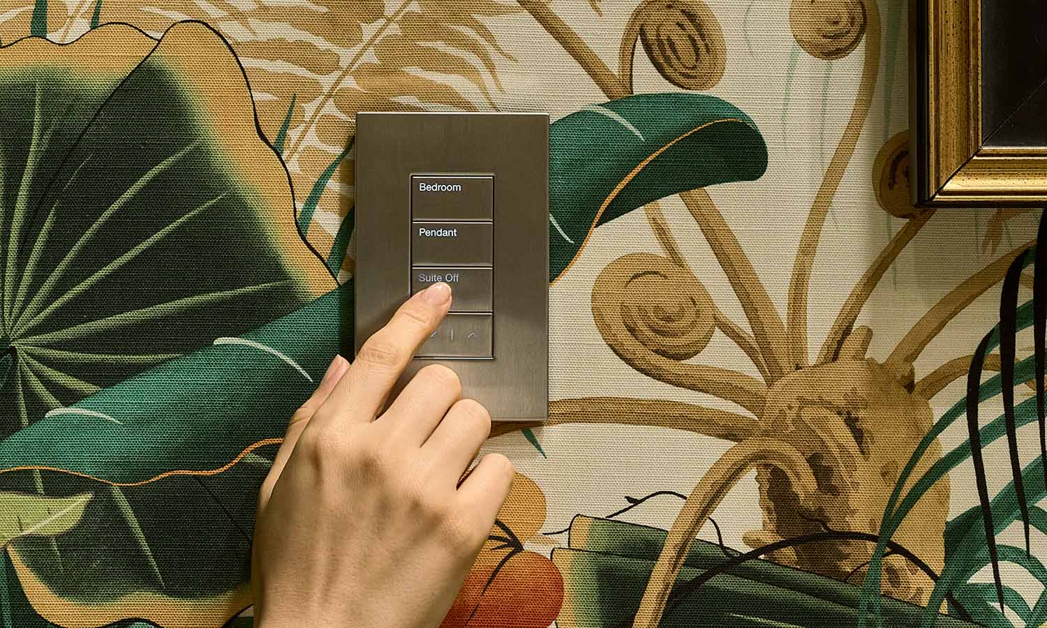 Hand pressing a silver Lutron Palladiom keypad on tropical wallpaper.