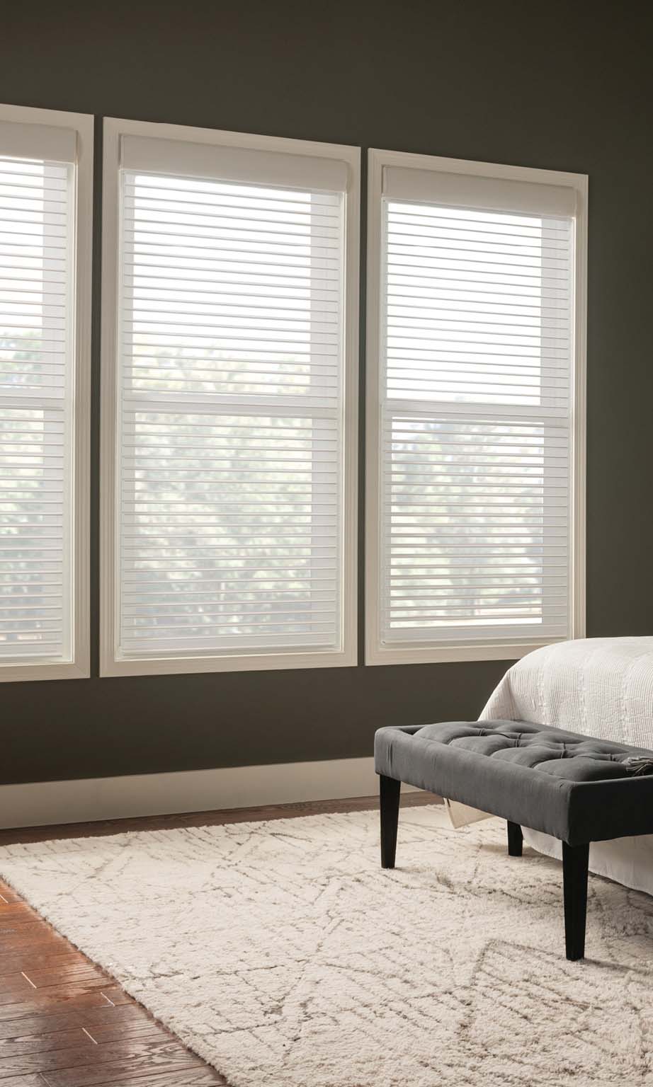 White Lutron automated wood blinds filtering light in a gray bedroom.