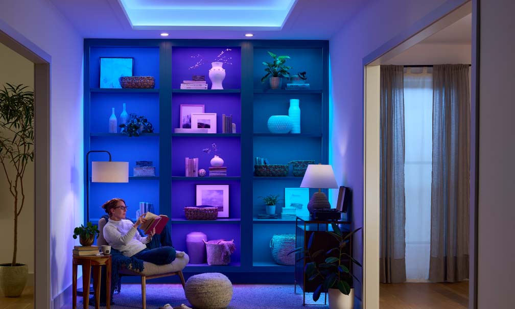 Woman reading near built-in bookshelves lit by blue Lutron Lumaris tape.