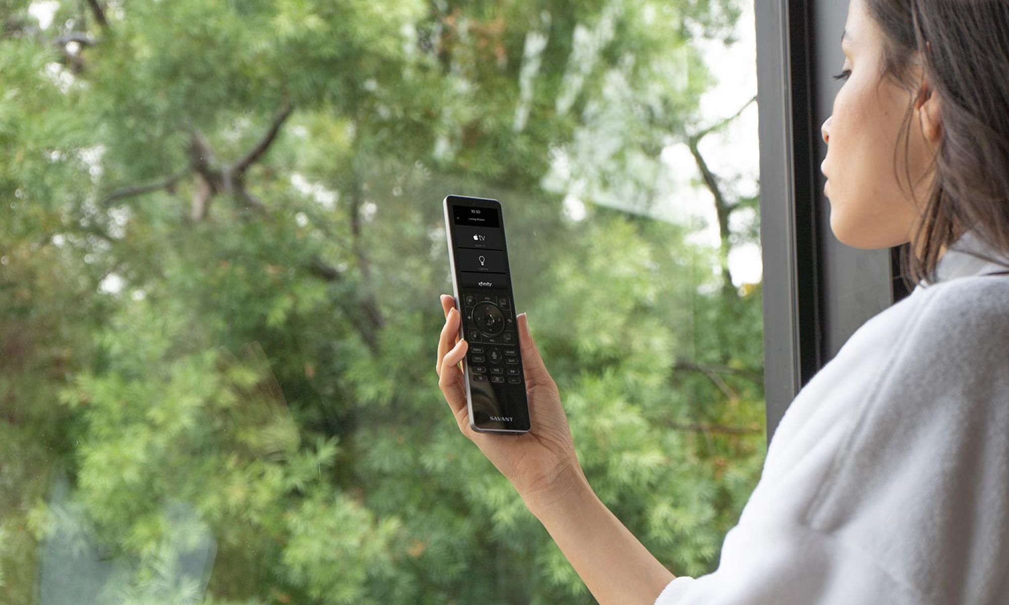 Person holding a sleek black smart home remote control near a window