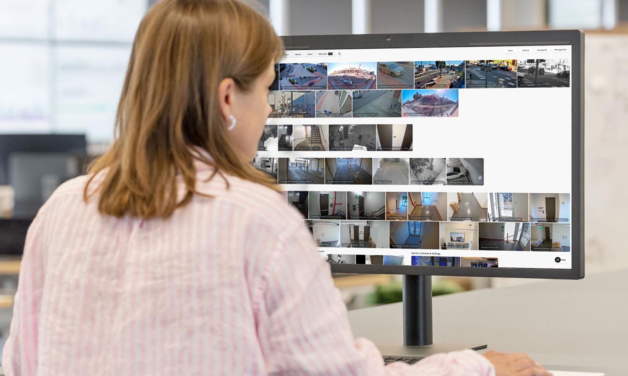 Woman viewing a grid of security camera feeds on a large computer monitor