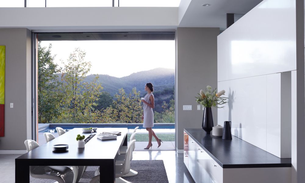 Modern luxury dining area opening to a poolside terrace, with a woman enjoying expansive mountain views.