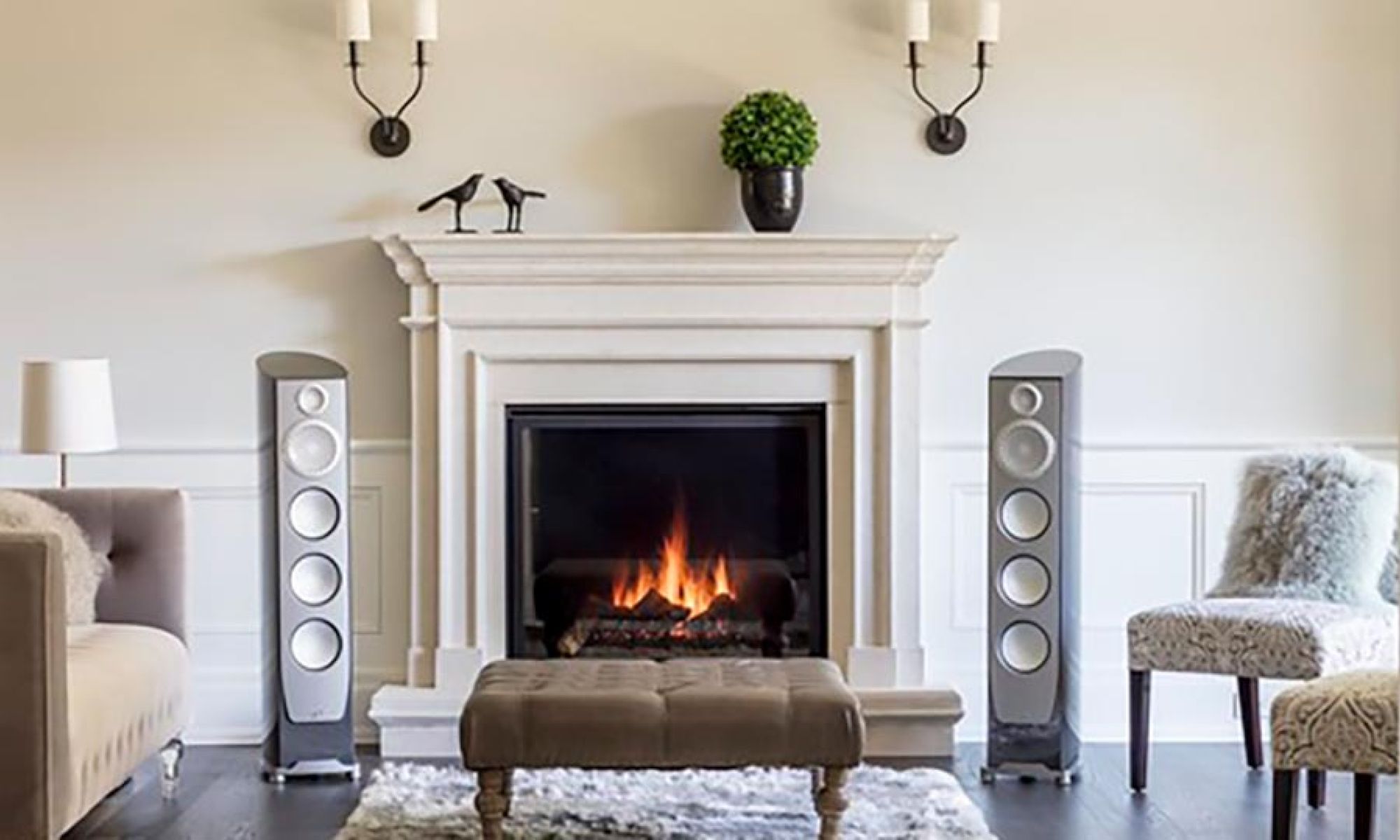Pair of tall silver floor-standing speakers flanking a white fireplace